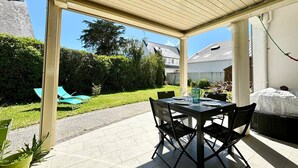 En udendørs patio med et bord og stole, et overdækket område og udsigt til en have samt nabohuse.