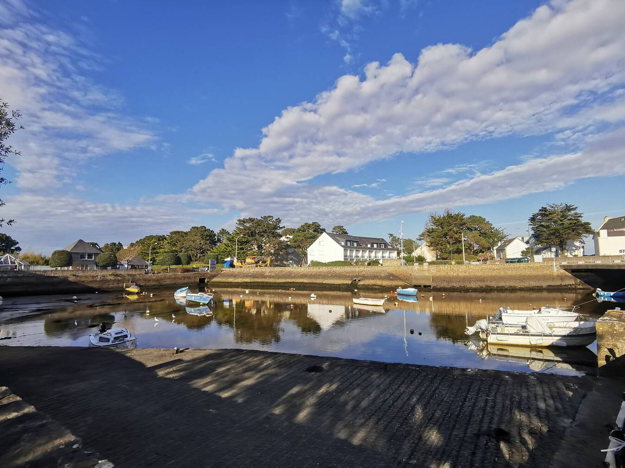 A calm river with boats docked, a bridge, and buildings along the riverbank.
