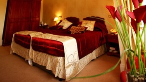 Quarto de hotel com uma cama grande, um candelabro, uma mesa de cabeceira e um vaso de flores.