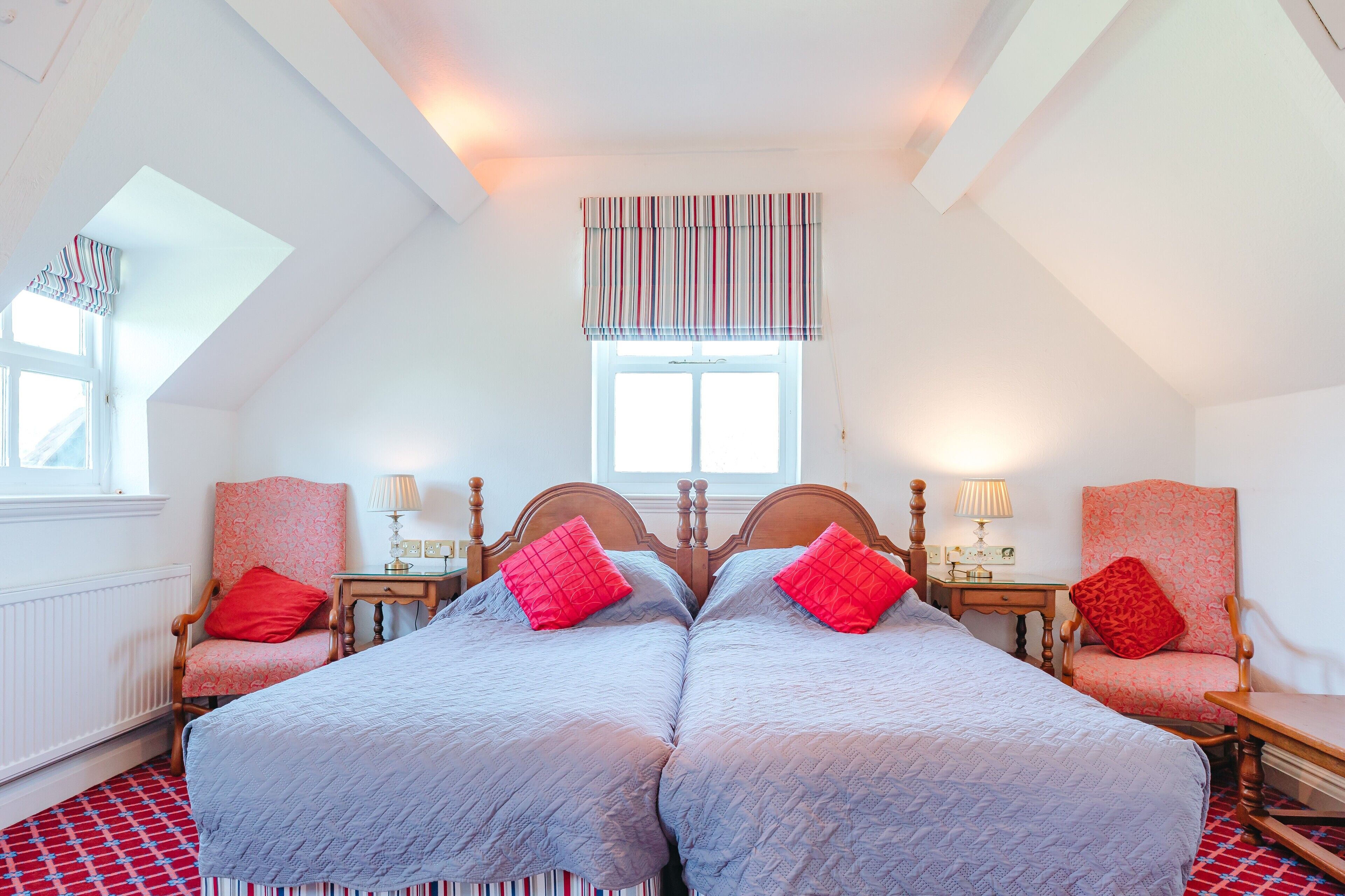 A bedroom with two beds, a window with a striped valance, a red and white patterned floor, and a wooden headboard.