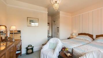 A hotel room with two beds, a wooden dresser, a chair, a small table with a fruit bowl, and a chandelier.