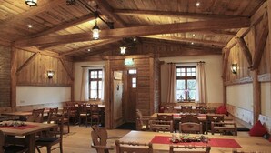 A rustic wooden interior with multiple dining tables and chairs, wooden beams on the ceiling, and windows with curtains. - Hotel Gasthaus Sonne (Peissenberg)
