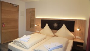 A double bed with two pillows and a folded towel on each side. There is a wooden wardrobe and a nightstand with a lamp. - Hotel Gasthaus Sonne (Peissenberg)