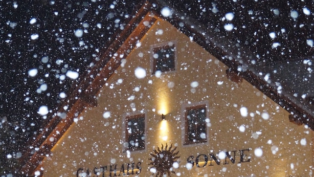 A building with the sign "CITILHUS SONNE" at night, illuminated by warm lights, with snow falling outside. - Hotel Gasthaus Sonne (Peissenberg)