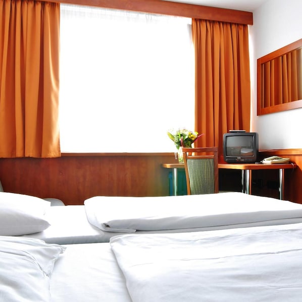 Une chambre d’hôtel avec deux lits, un bureau avec une télévision et une fenêtre avec des rideaux.