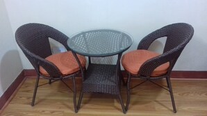 Una mesa pequeña y redonda con dos sillas de mimbre, cada una con un cojín.