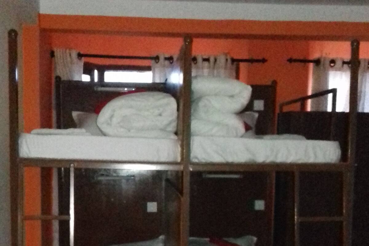A bunk bed room with three levels, wooden railings, and a window with curtains.