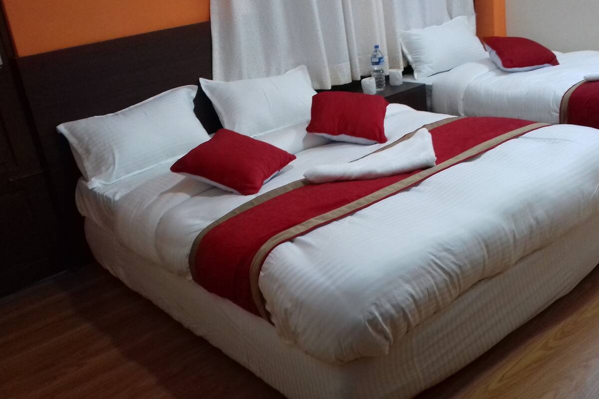 Two beds with white bedding and red accents, a wooden floor, and a white curtain in the background.