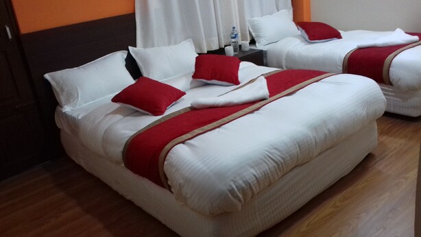 Dos camas con ropa de cama blanca y detalles rojos, piso de madera y una cortina blanca al fondo.
