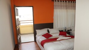 Una habitación de hotel con cama, mesita de noche, ventana con cortinas y puerta que da a un balcón.