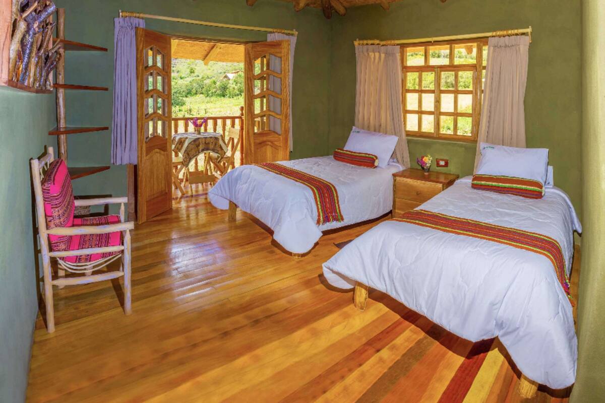 Habitación con dos camas, suelo de madera, una silla de madera y vista a zonas verdes.