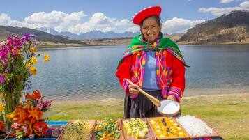A person serving food at a lakeside table with various dishes and a bouquet of flowers.