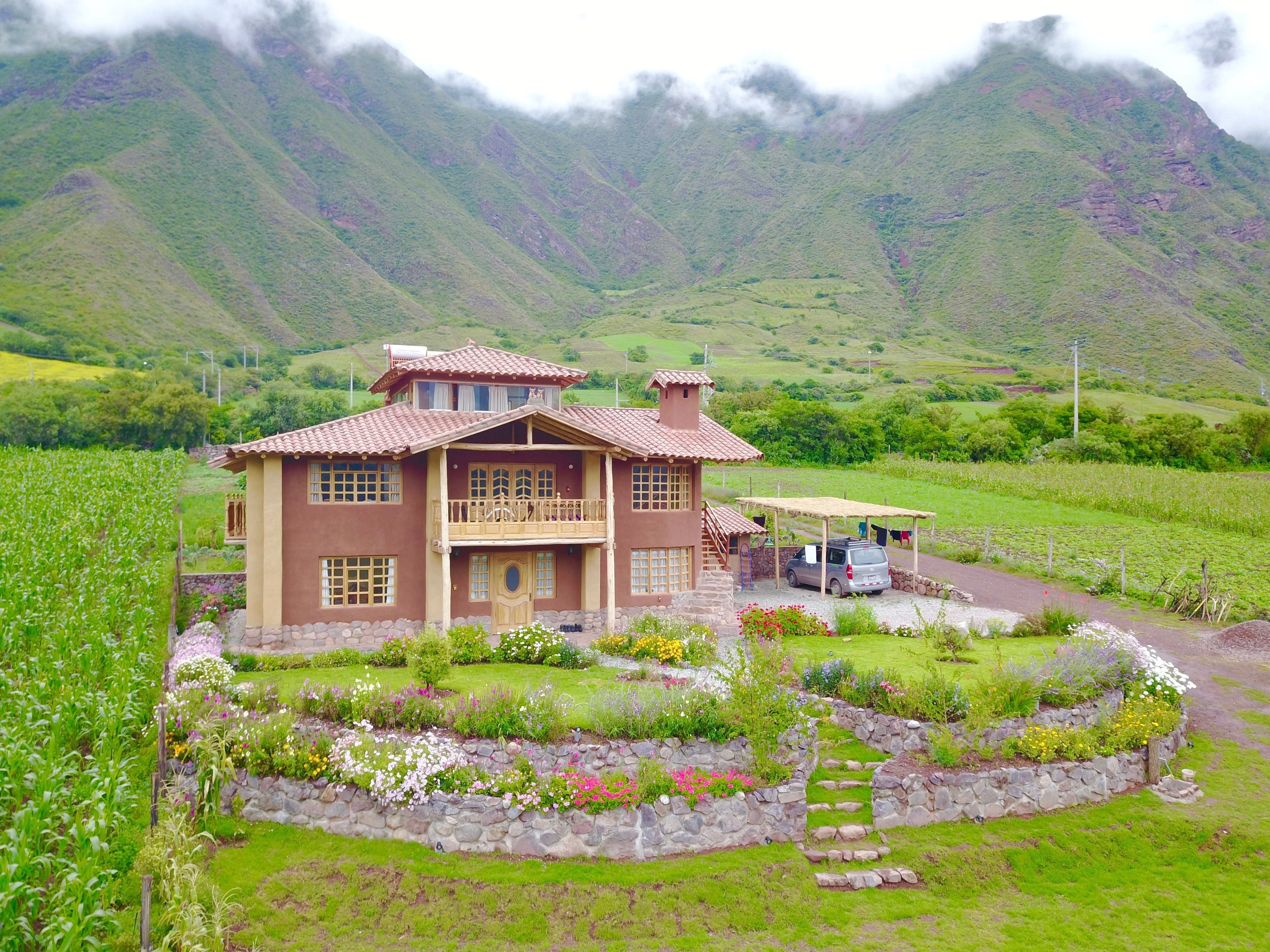 A two-story house with a balcony, surrounded by a well-maintained garden and a stone wall.