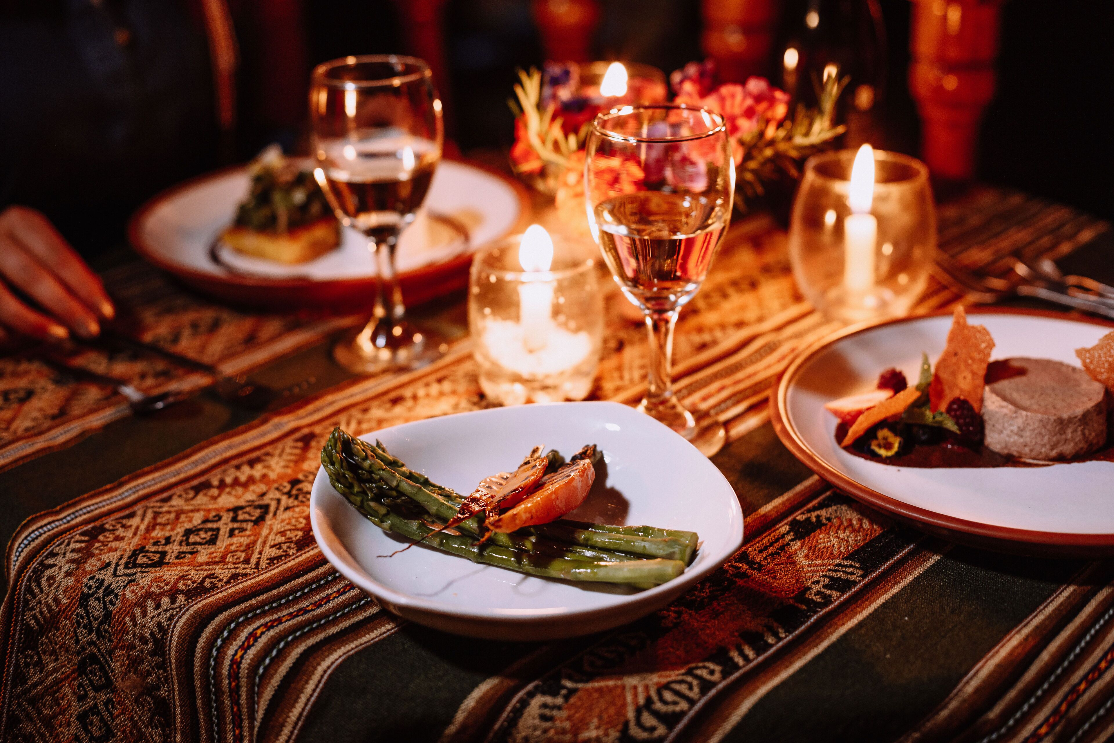 A dining table with plates of food, glasses of wine, and candles.