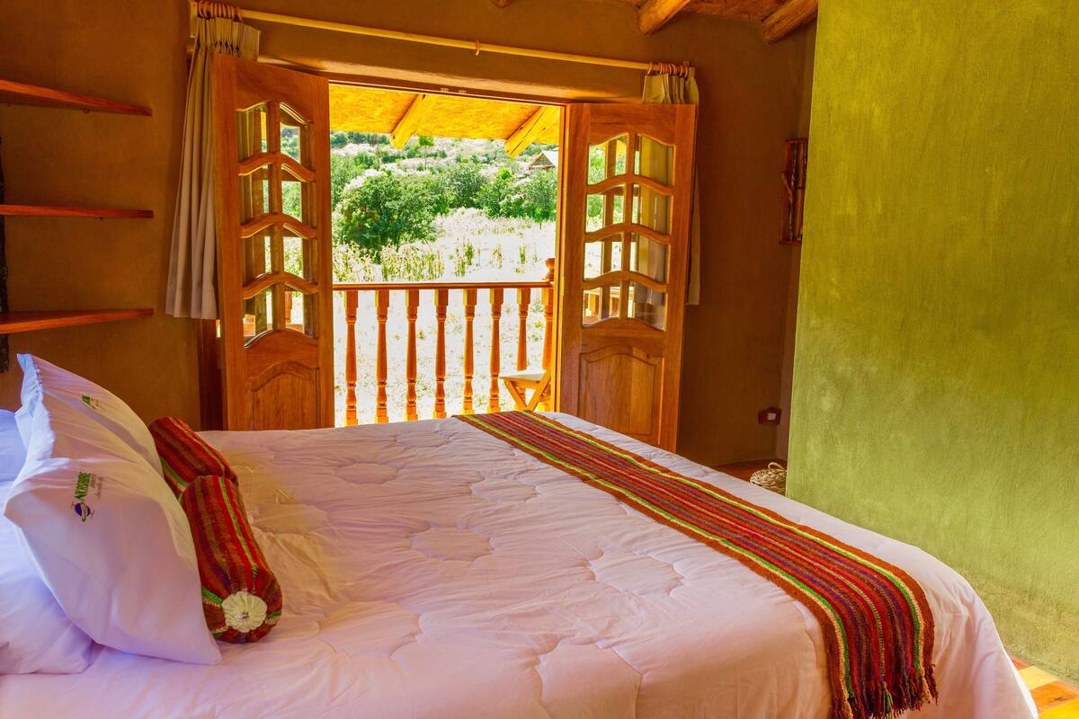 Un dormitorio con una cama grande, vistas a zonas verdes y un balcón con barandillas de madera.