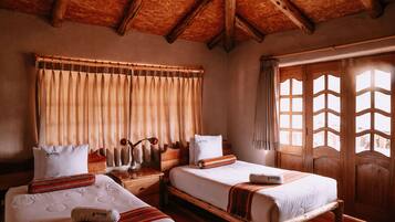 Una habitación con dos camas, cabeceros de madera, techo de madera y un ventanal grande con cortinas.