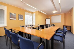 Een congreszaal met een lange tafel, blauwe stoelen, een whiteboard en ingelijste foto's aan de muur.