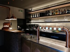 Een barruimte met een koperen bierkraan, flessenkasten vol drank en een koffiemachine.