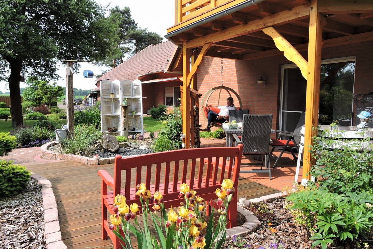A wooden deck with a red bench, yellow flowers, and a swing chair.