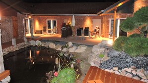 A brick building with a covered patio area, a small pond, and outdoor seating.