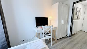 Una habitación de hotel moderna con una cama, un escritorio con televisor, una silla y un armario.
