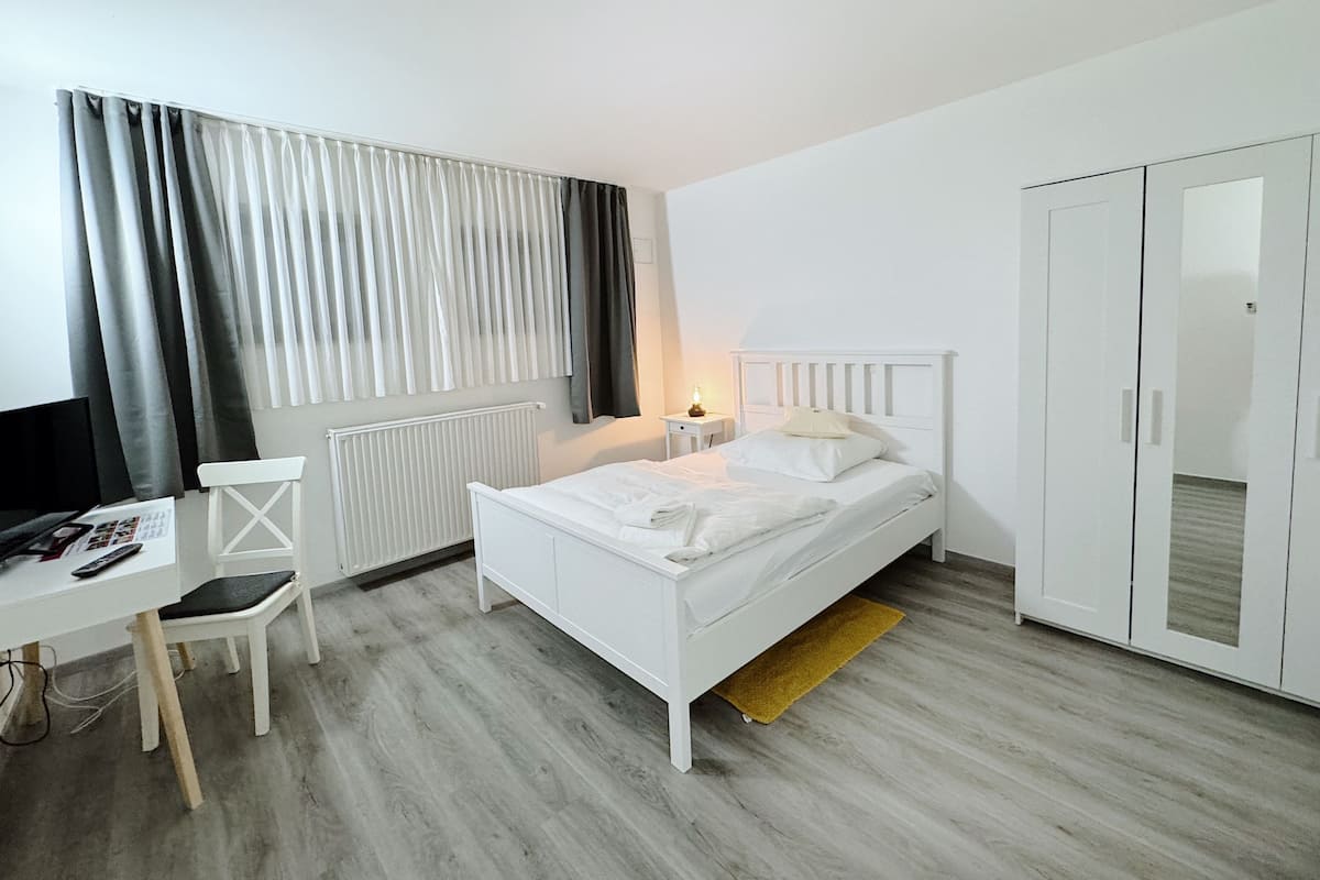 A bedroom with a bed, a desk, a chair, a wardrobe, and a radiator.