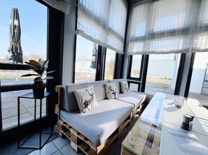 A modern living room with a sofa, cushions, a potted plant, and a glass table. - Regiohotel Wittekind Burg (Burg)