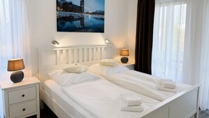 A neatly made bed with white linens and pillows, a bedside table with a lamp, and a painting of a cityscape above the bed. - Regiohotel Wittekind Burg (Burg)