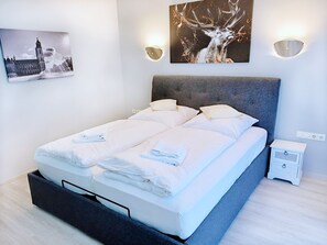 Una habitación de hotel moderna con una cama grande, dos mesitas de noche, una lámpara de pared e imagen enmarcada de un ciervo.