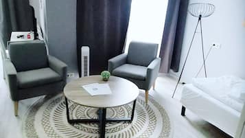 A modern room with two grey armchairs, a round coffee table with a patterned rug, a small potted plant, a white sofa, and a floor lamp.