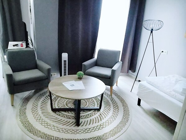 A modern room with two grey armchairs, a round coffee table with a patterned rug, a small potted plant, a white sofa, and a floor lamp.