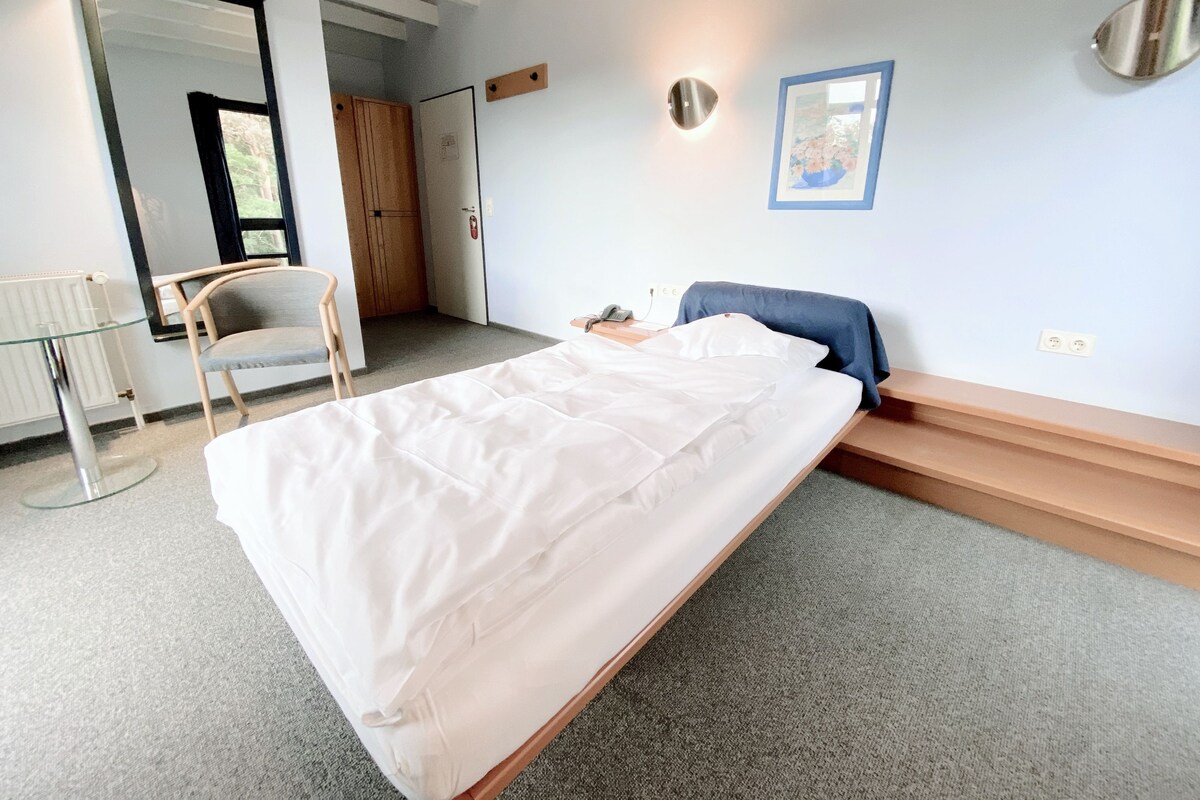 A bedroom with a bed, a chair, a desk, a mirror, and a door.