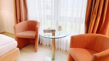 Quarto de hotel com duas poltronas laranja, uma mesa de vidro e uma cama.