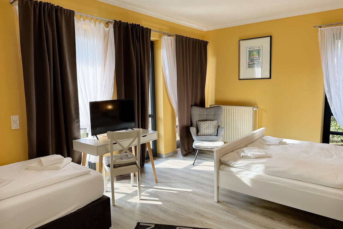 A hotel room with two beds, a desk with a TV, a chair, and a radiator.