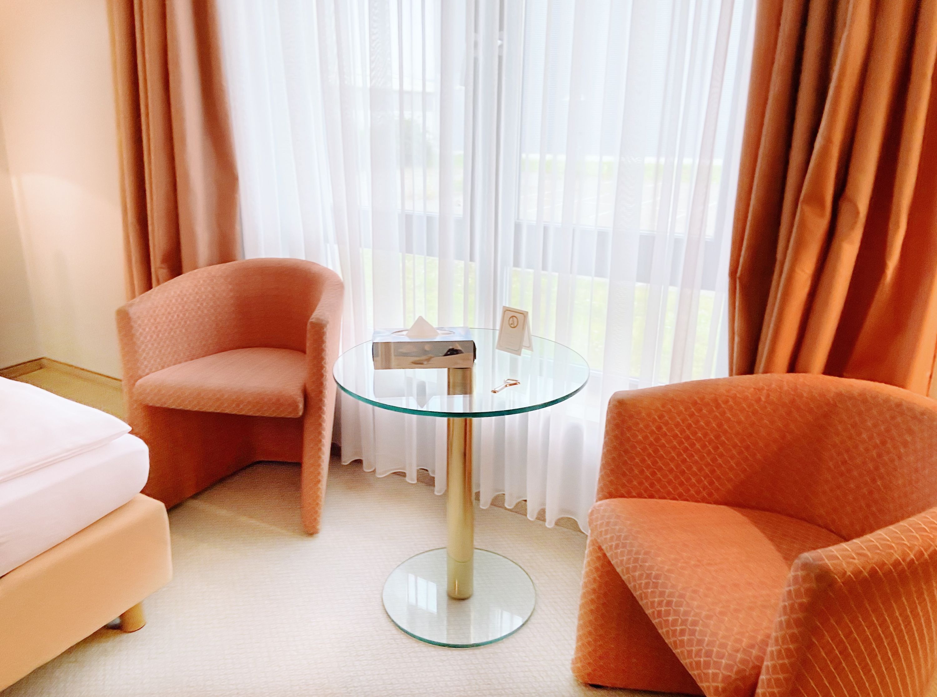 Ein Hotelzimmer mit zwei orangefarbenen Sesseln, einem Glastisch und einem Bett.