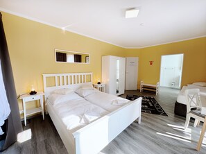 A hotel room with a double bed, a bedside table with a lamp, a wardrobe, a bench, and a door leading to a bathroom. - Regiohotel Wittekind Burg (Burg)
