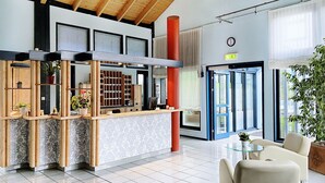 A reception area with a wooden reception desk, a clock on the wall, and a large window with blinds. - Regiohotel Wittekind Burg (Burg)