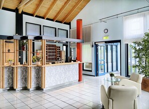 A reception area with a wooden reception desk, a clock on the wall, and a large window with blinds. - Regiohotel Wittekind Burg (Burg)