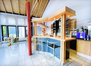 A modern bar area with a counter, stools, and a coffee machine.