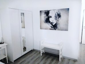 A modern room with a white wardrobe, a bench, and a large abstract painting on the wall.