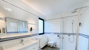 A modern bathroom with a large mirror, white vanity, and a glass-enclosed shower. - Regiohotel Wittekind Burg (Burg)