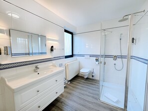 A modern bathroom with a large mirror, white vanity, and a glass-enclosed shower. - Regiohotel Wittekind Burg (Burg)