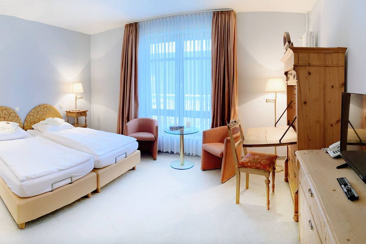 A hotel room with a double bed, a desk with a chair, a television, and a wardrobe.