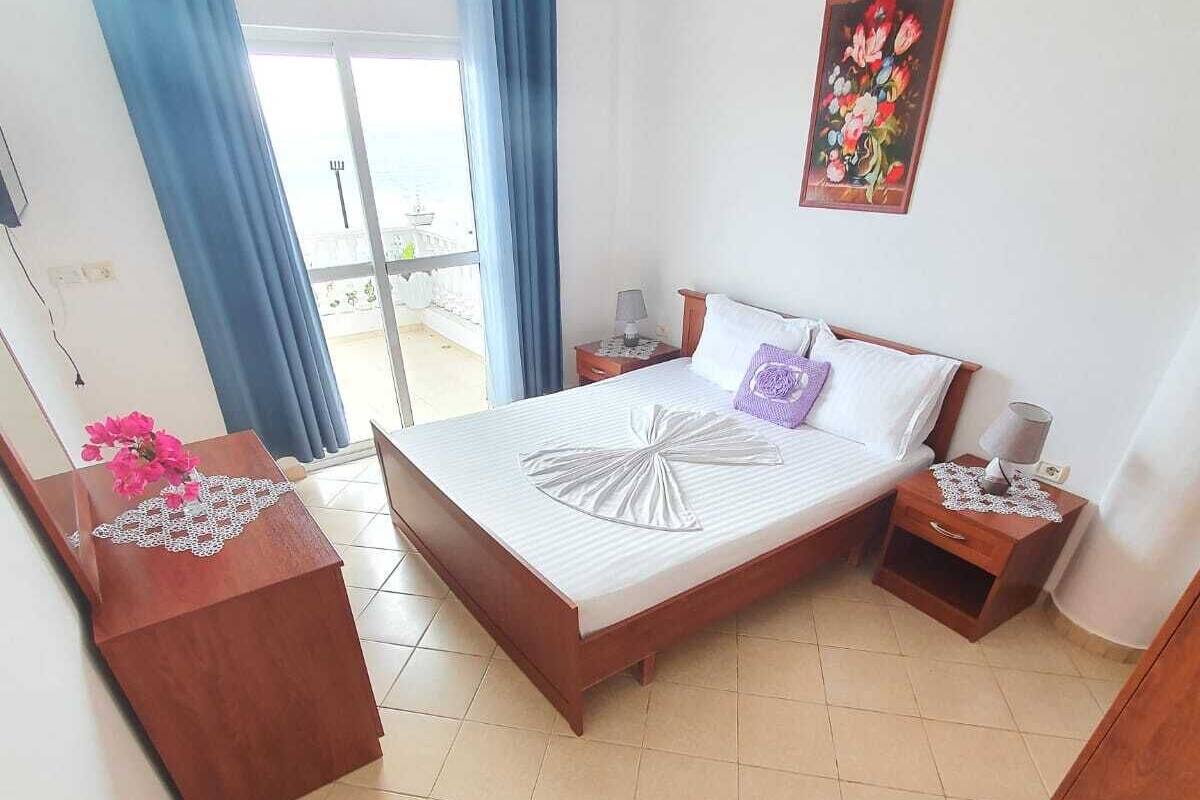 A bedroom with a bed, a nightstand, a dresser, a window with curtains, and a wall-mounted air conditioner.