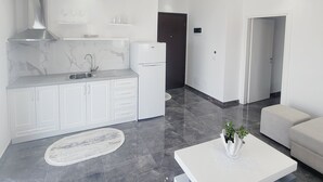 A modern kitchen with white cabinetry, a stainless steel range hood, and a white refrigerator. - Makla Apartaments (Sarandë)