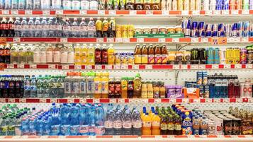 Ein Regalfach in einem Supermarkt, gefüllt mit verschiedenen Getränken, darunter Wasser, Limonade und Energydrinks.