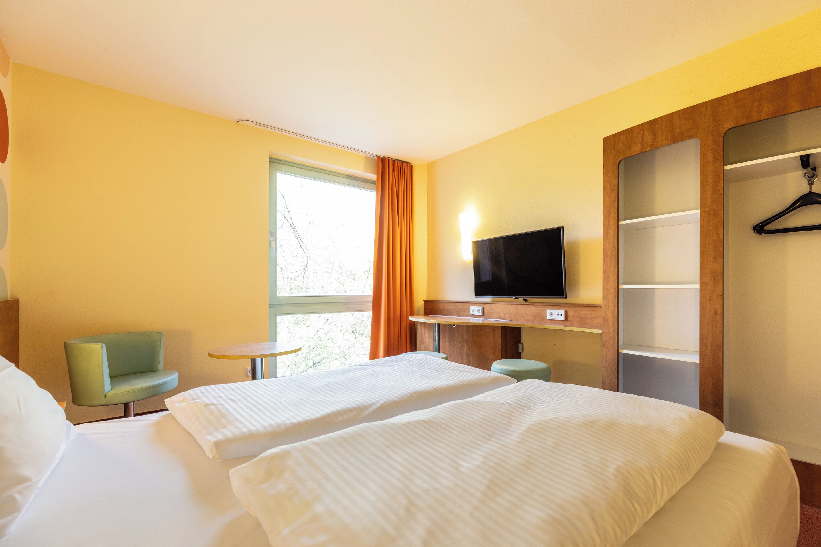 Une chambre d’hôtel avec deux lits, une télévision, une petite table, une chaise et une armoire.
