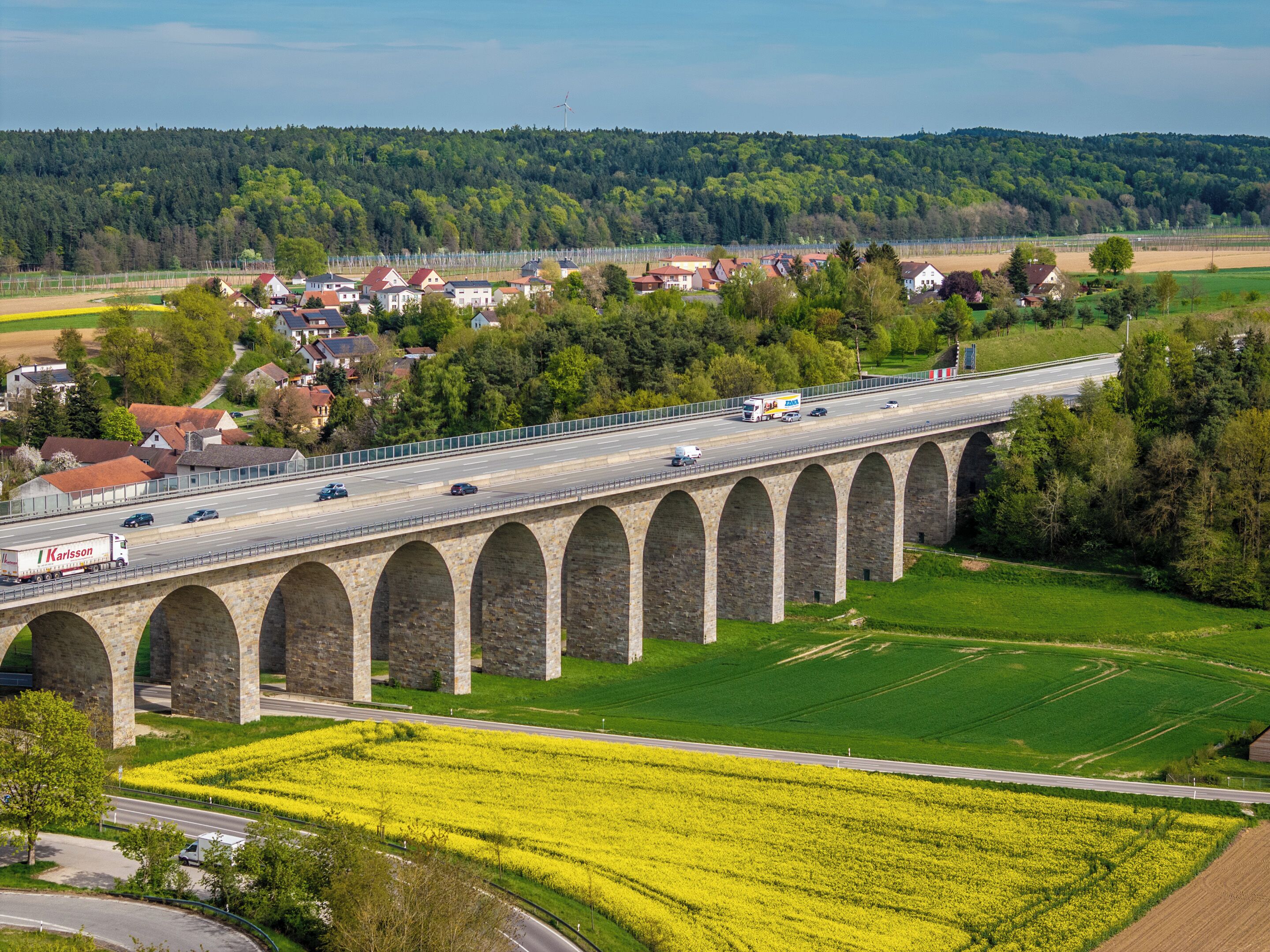 A stone viaduct with multiple arches over a road, surrounded by green fields and a small town in the background.