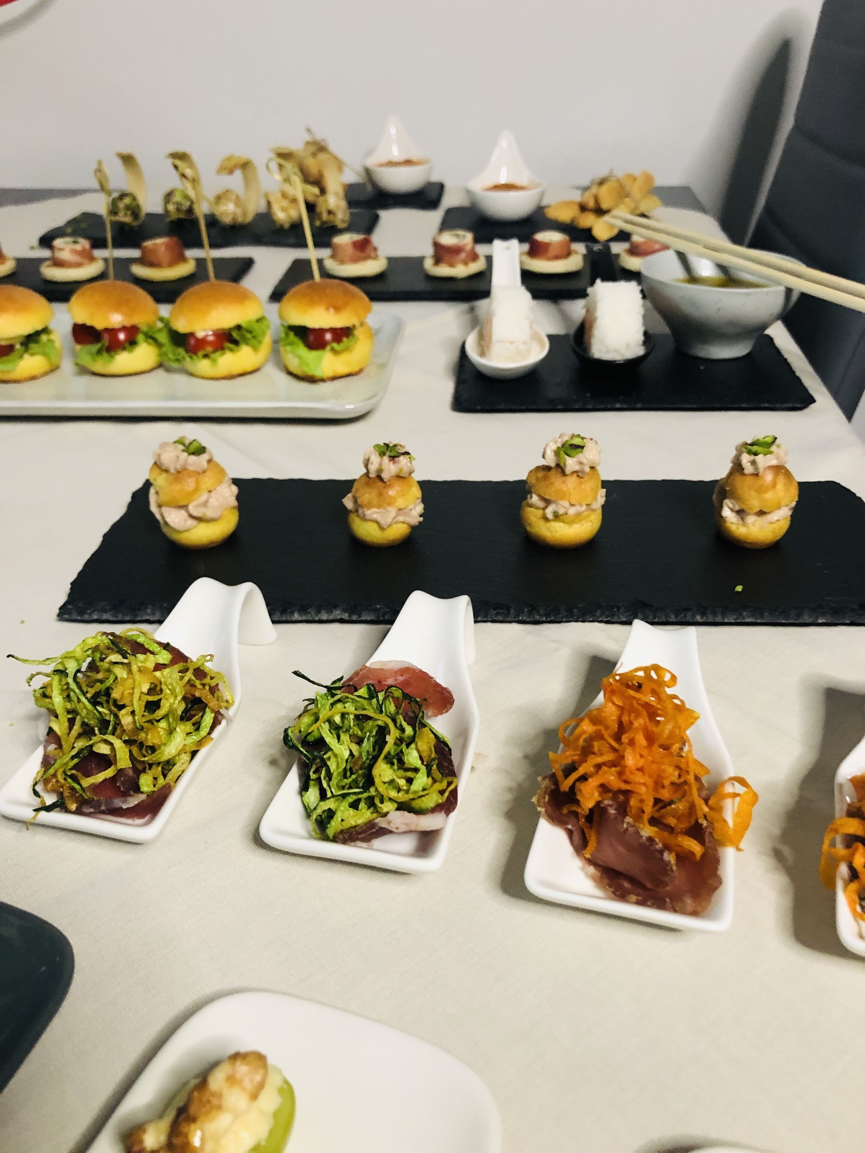 Verschiedene Vorspeisen sind auf einem Tisch angerichtet, darunter kleine Sandwiches, Spieße und reichhaltig dekorierte Gerichte.