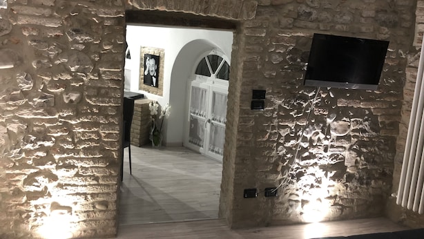 Un pasillo con paredes de piedra, un televisor montado en la pared, una puerta blanca y un cuadro enmarcado.